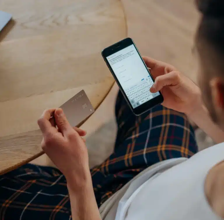 a person sitting on a couch holds a credit card in one hand and a smart phone in the other