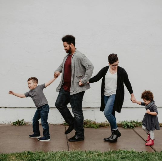 a family of 4 all walking in a line holding hands beside a building