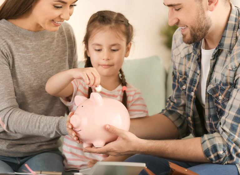 a young girl is dropping a quarter into a piggy bank held by her mother and father who sit next to her on a couch