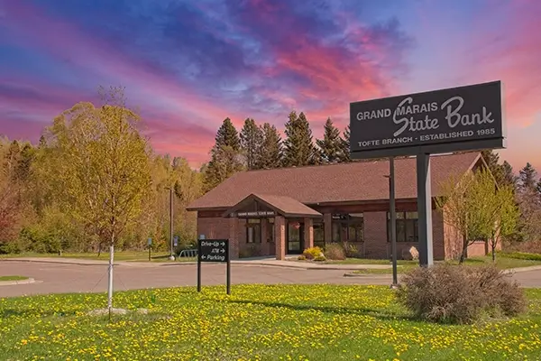 exterior building of grand marais state bank's tofte location with bright pink and blue sunset in background