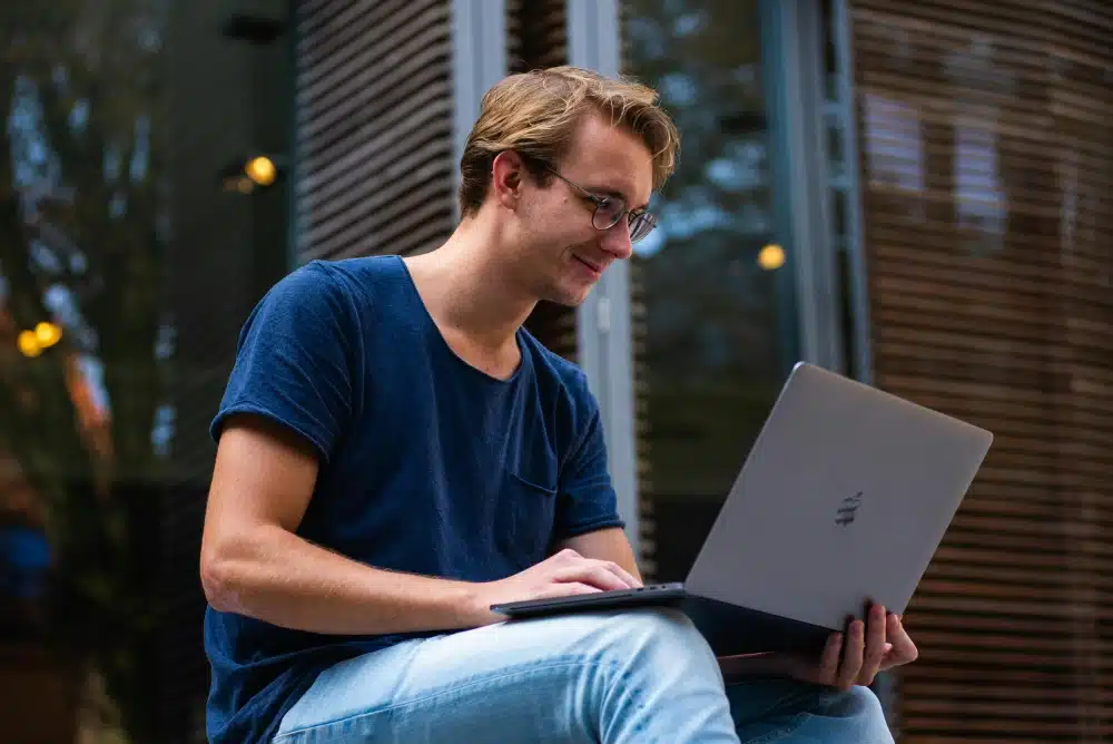 a young map sitting outside holding a laptop on his knees